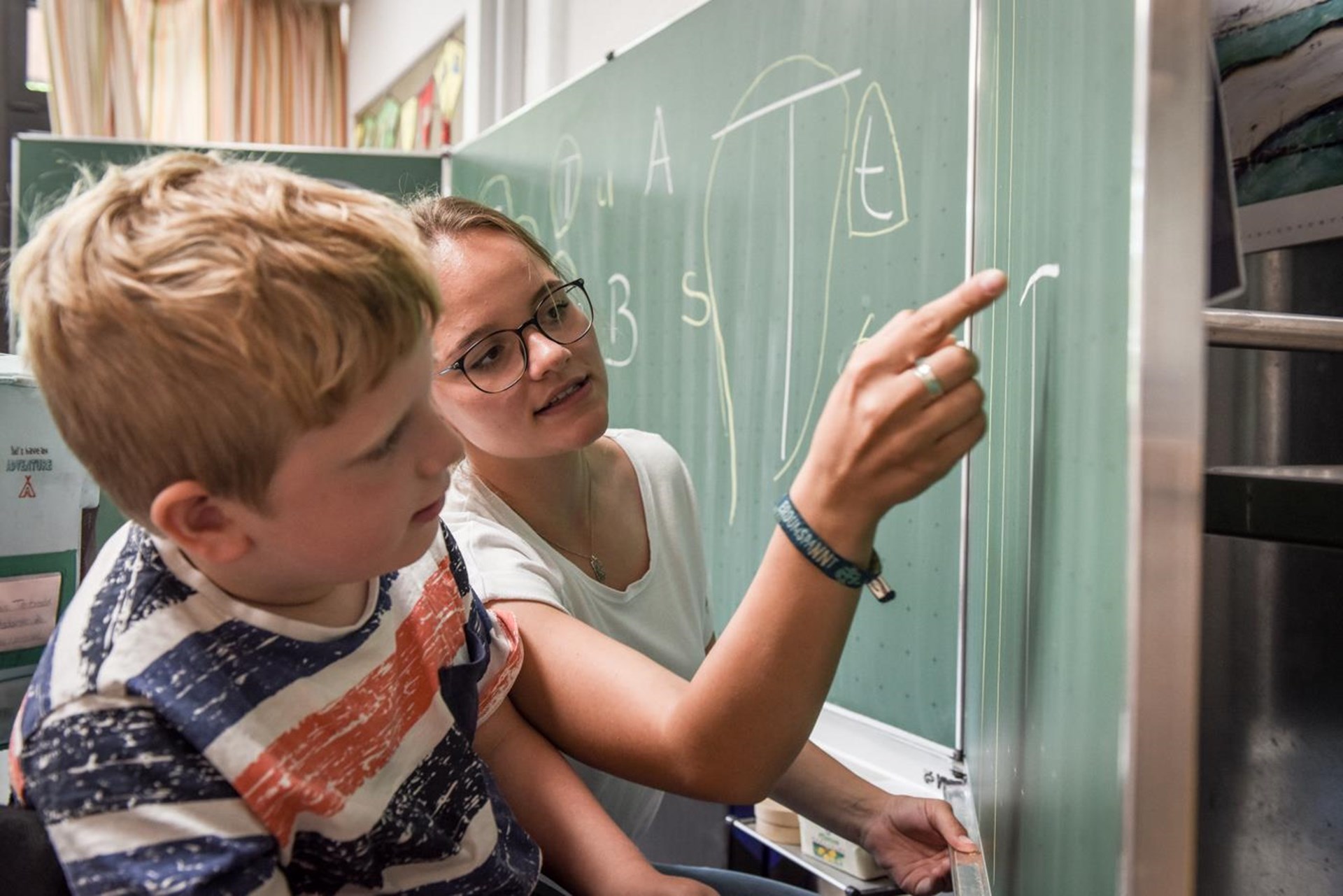 Freiwillige erklärt Jungen mit Behinderung etwas an einer Tafel