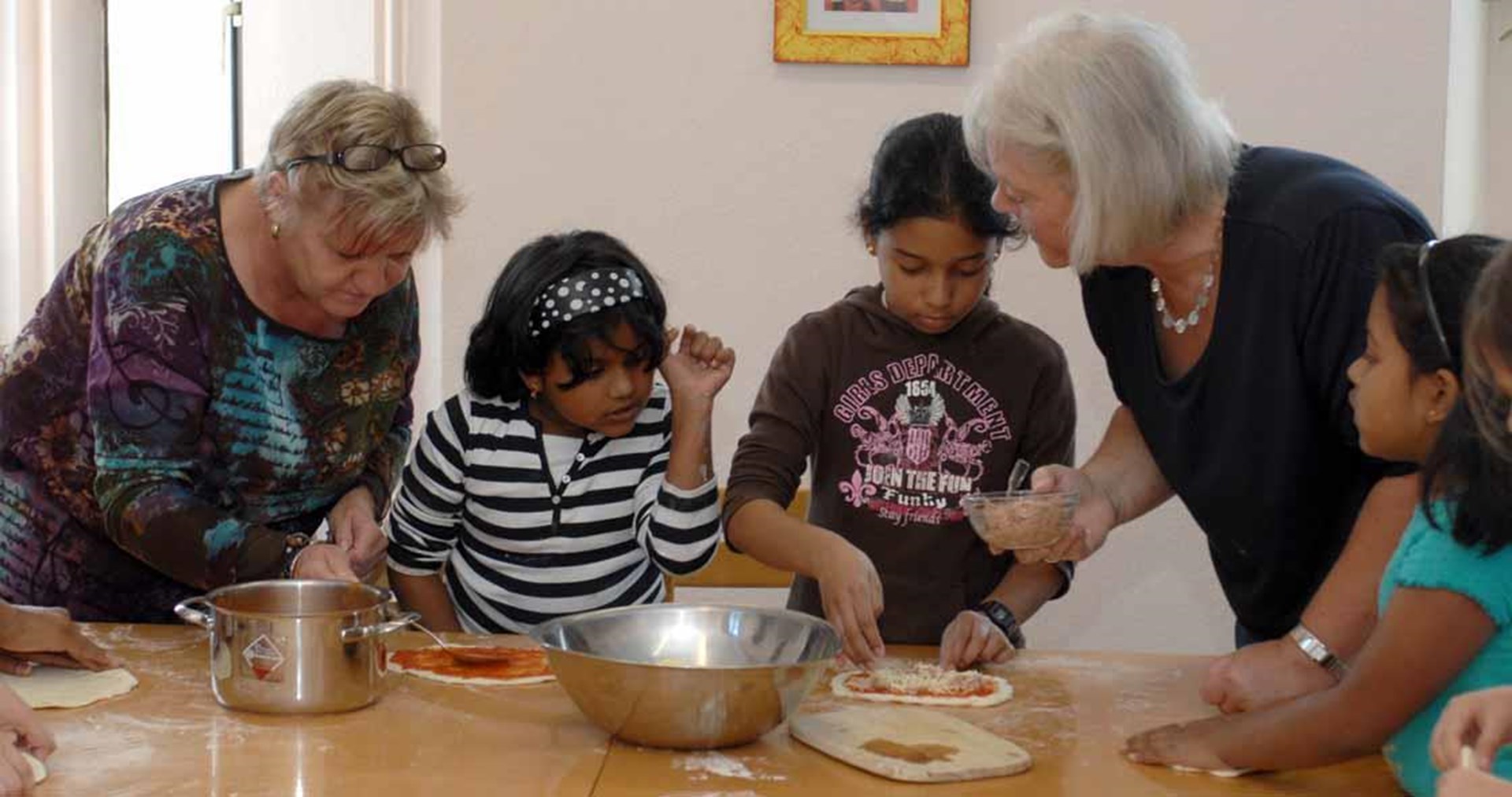 zwei Ehrenamtliche backen Pizza mit Kindern mit Migrationshintergrund