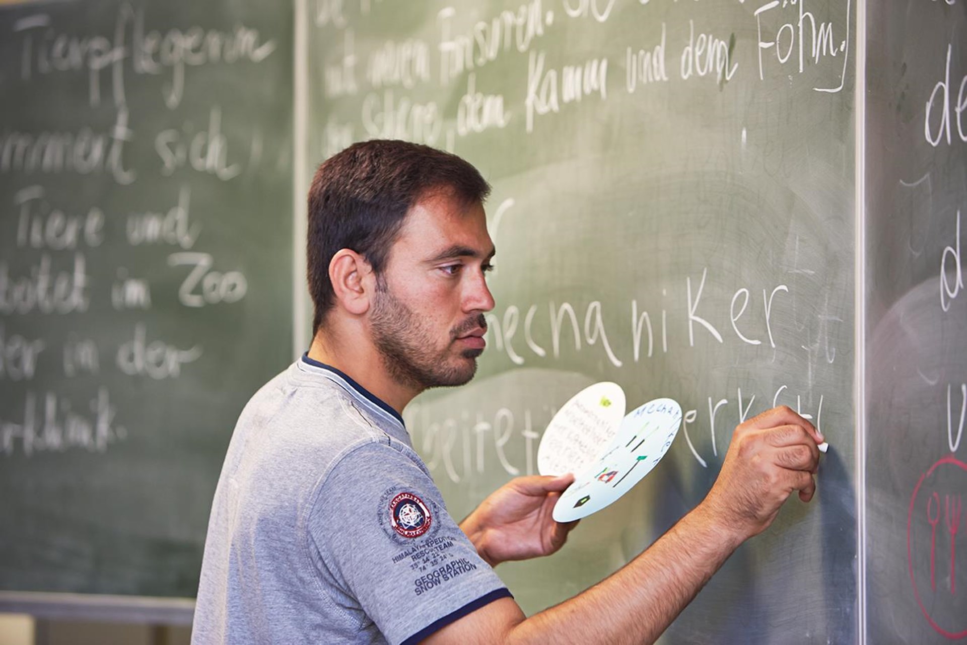 Mann steht an Schultafel mit Kreide.