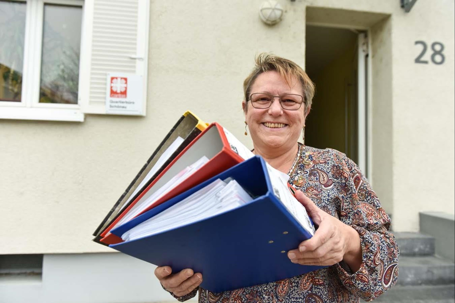 Eine Quartiersarbeiterin steht vor dem Quartiersbüro der Caritas und hält Akten in der Hand
